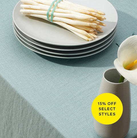 Stack of plates with asparagus on a light blue tablecloth, featuring a promotional sticker.